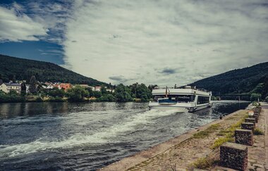 Ein weißess Ausflugsschiff welches auf einem Fluss fährt. Auf der linken Seite am Ufer sieht man eine Stadt. Neckargemünd im Odenwald. | © Touristikgemeinschaft Odenwald e.V.