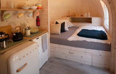 Der Innenraum eines Holziglus mit Bett. Im Vordergrund auf der linken Seite eine kleine Küchenzeile.