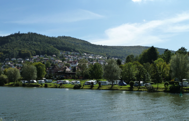 Im Vordergrund ist ein Fluß zu sehen (Neckar). Am Ufer des Flusses ist ein Campingplatz mit einer Reihe von Wohnwägen, mit einem bewaldeten Berg im Hintergrund. Eberbach im Odenwald. | © Campingpark Eberbach