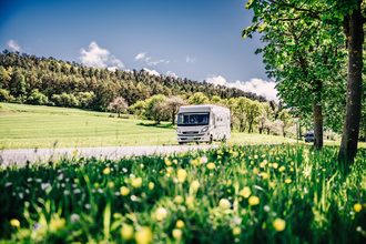 Weißes Wohnmobil fährt auf einer Strasse. Im Vordergrund ist eine Blumenwiese im Hintergrund eine Steuobstwiese mit angrenzendem Wald. | Odenwald | © Touristikgemeinschaft Odenwald e.V.