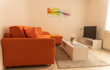 orangefarbene Couch mit kleinem weißen Couchtisch und in der Ecke steht ein Fernseher | © Neckar-Zaber-Tourismus e.V.