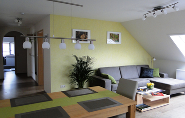 Esstisch mit mind. einem Stuhl, große graue Couch mit Couchtisch an einer gelben Wand | © Neckar-Zaber-Tourismus e.V.