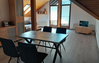 Blick in den Wohnraum der Ferienwohnung mit Esstisch, Fernseher und Sofa | © E. Hügler