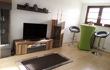 Großes Wohnzimmer mit Fernseher, einem Hochtisch und zwei Barhockern und eine Vitrine