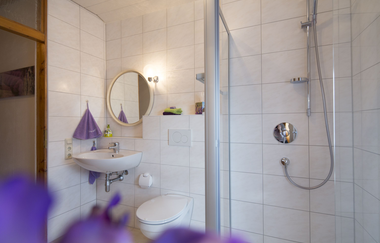 Badezimmer mit weißen Fliesen, große Dusche, Toilette, Waschbecken und ein runter Spiegel | © Neckar-Zaber-Tourismus e.V.