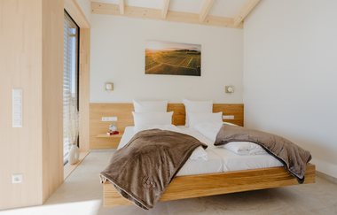 Doppelbett aus hellem Holz mit weißem Bettbezug und brauner Tagesdecke | © Weingut Becker, Malsch