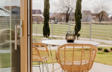 Blick auf gepflasterte Terrasse mit Tisch und zwei Korbstühlen, im Hintergrund Wiesengelände und einige Häuser in der Ferne | © Weingut Becker