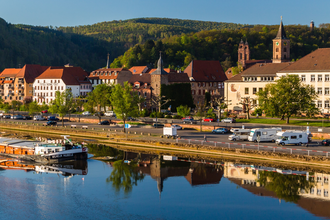 Im Vordergrund ist ein Fluß mit einem Binnenschiff. Dahinter am Ufer ist direkt ein Wohnmobilstellplatz mit 3 Wohnmobilen. Im Hintergrund ist eine Stadt mit Häusern und einer Kirche. Eberbach im Odenwald. | © Stadtverwaltung Eberbach