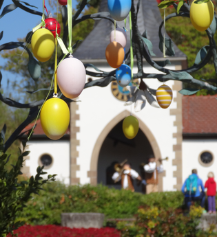 Bunte Ostereier hängen an einem Baum vor einem Gebäude mit Menschen im Hintergrund. | © Erlebnispark Tripsdrill