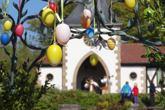 Bunte Ostereier hängen an einem Baum vor einem Gebäude mit Menschen im Hintergrund. | © Erlebnispark Tripsdrill