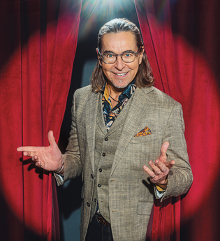 Künstler im Anzug steht vor einem roten Bühnenvorhang