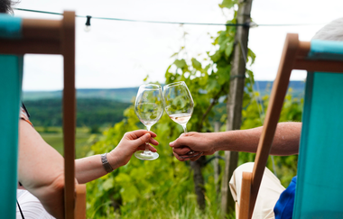 Zwei Liegestühle in den Weinbergen mit zwei Personen, die sich mit Weingläsern zu prosten | © Weingäe Stromberg-Zabergäu