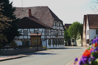 Fachwerkhaus mit rotem Ziegeldach und Schild 'Zum Löwen' an einer ruhigen Straße, rechts weitere Häuser und Bäume. | © Landratsamt Rhein-Neckar-Kreis