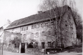 Schwarz-Weiß-Foto eines historischen Gebäudes hinter einer Steinmauer | © Unbekannt