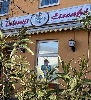 Außenansicht des Eiscafés mit Schild und grünen Pflanzen