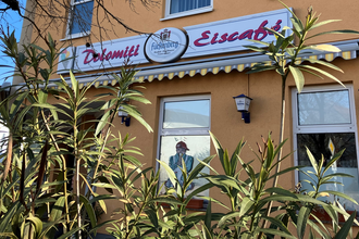 Außenansicht des Eiscafés mit Schild und grünen Pflanzen