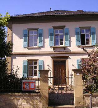 Front des zweistöckigen Dekanatsgebäudes mit blauen Fensterläden und kleinem Vorgarten | © Stadt Sinsheim