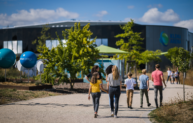 Eine Gruppe Menschen läuft auf einem Steinweg durch den angelegten Außenbereich der Klima Arena | © KLIMA ARENA Sinsheim