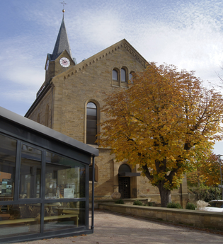 Blick auf die Westseite der Mauritiuskirche. Vor dem Eingang steht ein Baum mit bunten Blättern. | © Neckar-Zaber-Tourismus