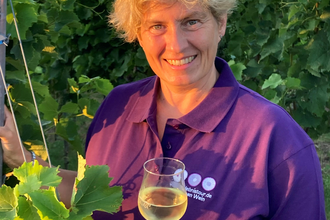 Nicole Betz mit lila Shirt der WeinErlebnisFührer und Weinglas in der Hand zwischen Weinreben | © Nicole Betz