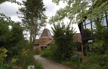 gepflasterter schmaler Weg mit Sträuchern am Rande des Wegs; im Hintergrund ist das ökumenische Kirchenzentrum  Arche zu sehen | © Stadt Neckargemünd