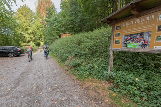 Zwei Radfahrer mit Schautafel des Waldlehrpfads und Bäume
