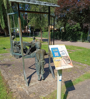 Schild der Weitersehen-Station in Hockenheim vor einer Statue in dem 3 Personen beim Tabakdrehen dargestellt sind | © Landratsamt Rhein-Neckar-Kreis