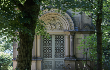 Reich verzierte steinere Eingangstür eines Mausoleums unter alten Bäumen. | © Gernot Wagner