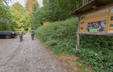 Zwei Radfahrer mit Schautafel des Waldlehrpfads und Bäume