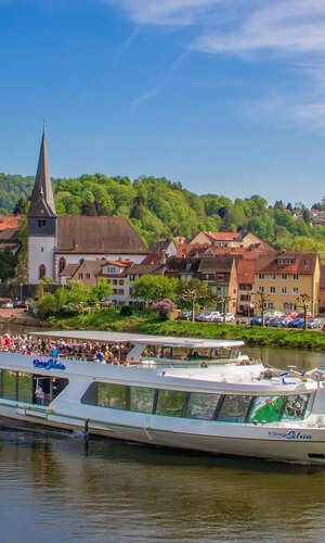 Fahrgastschiff auf dem Fluss vor der Stadt Neckargemünd mit historischen Gebäuden und bewaldeten Hügeln im Hintergrund. | © Stadt Neckargemünd, Foto Jens Hertel