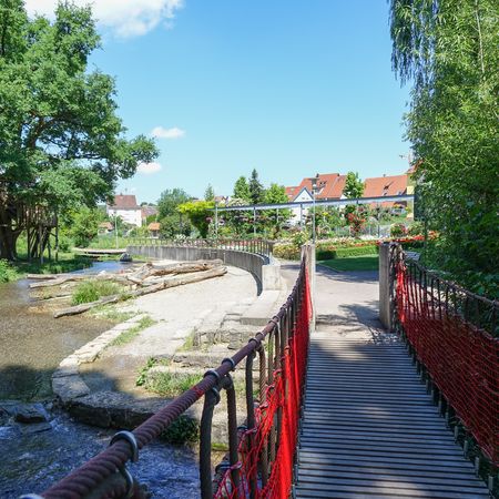 Hängebrücke mit Blick auf Blumen, Fluss und Spielplatz im Rathauspark