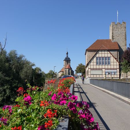 Brücke mit Blumen und Radfahrern und Rathausburg im Hintergrund